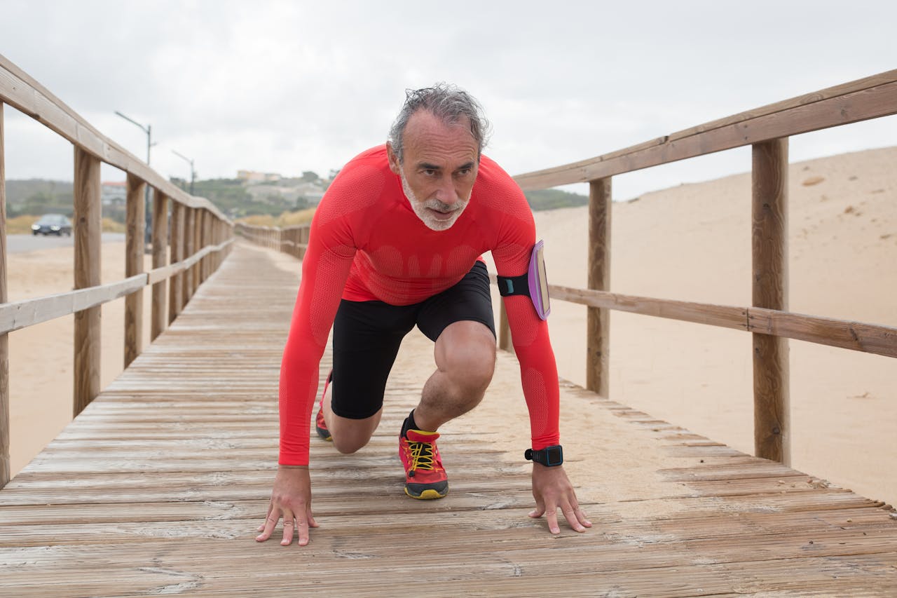 Active senior man in red preparing for a run on a scenic wooden pathway at the beach.